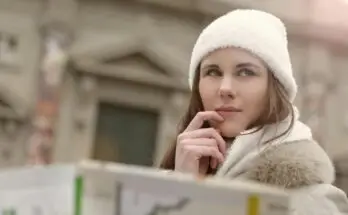 Concentrated female in warm hat and coat looking for right way while standing with map in street